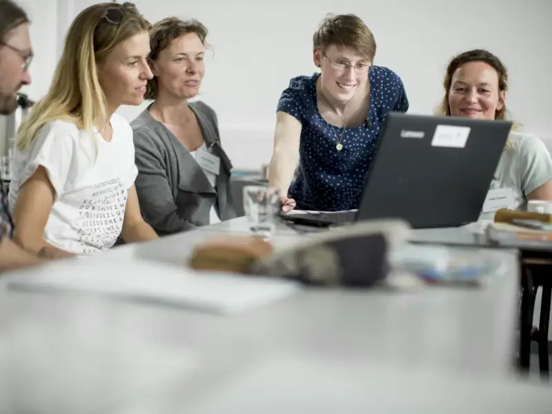 Mehrere Personen schauen gemeinsam auf einen Laptop-Bildschirm. Alle lächeln