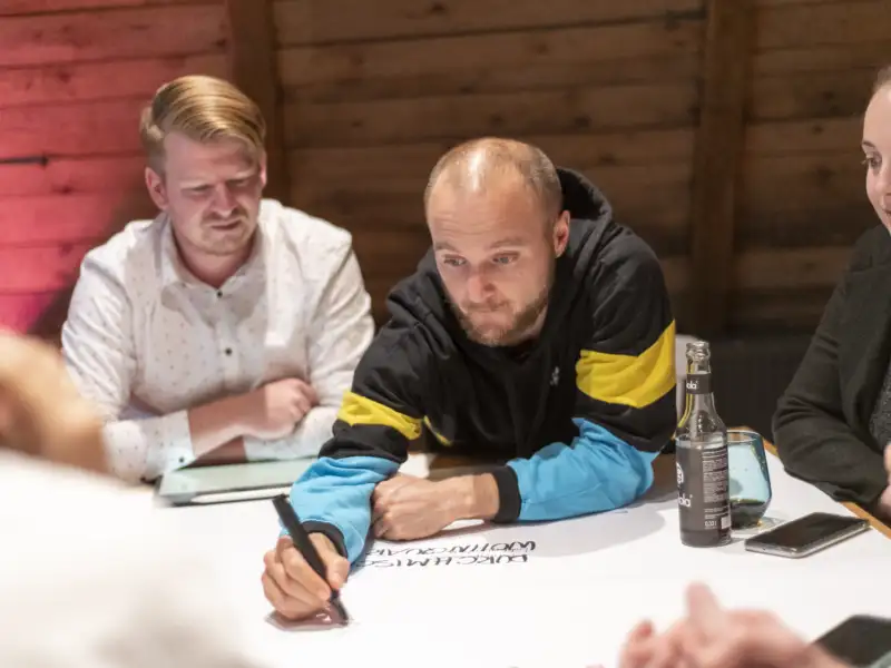 Mehrere Personen arbeiten gemeinsam an einem Tisch zusammen auf einem großen Blatt Papier.