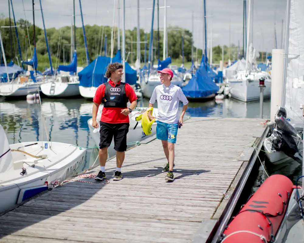 Zwei Männer laufen einen Boots-Steg entlang und lachen.