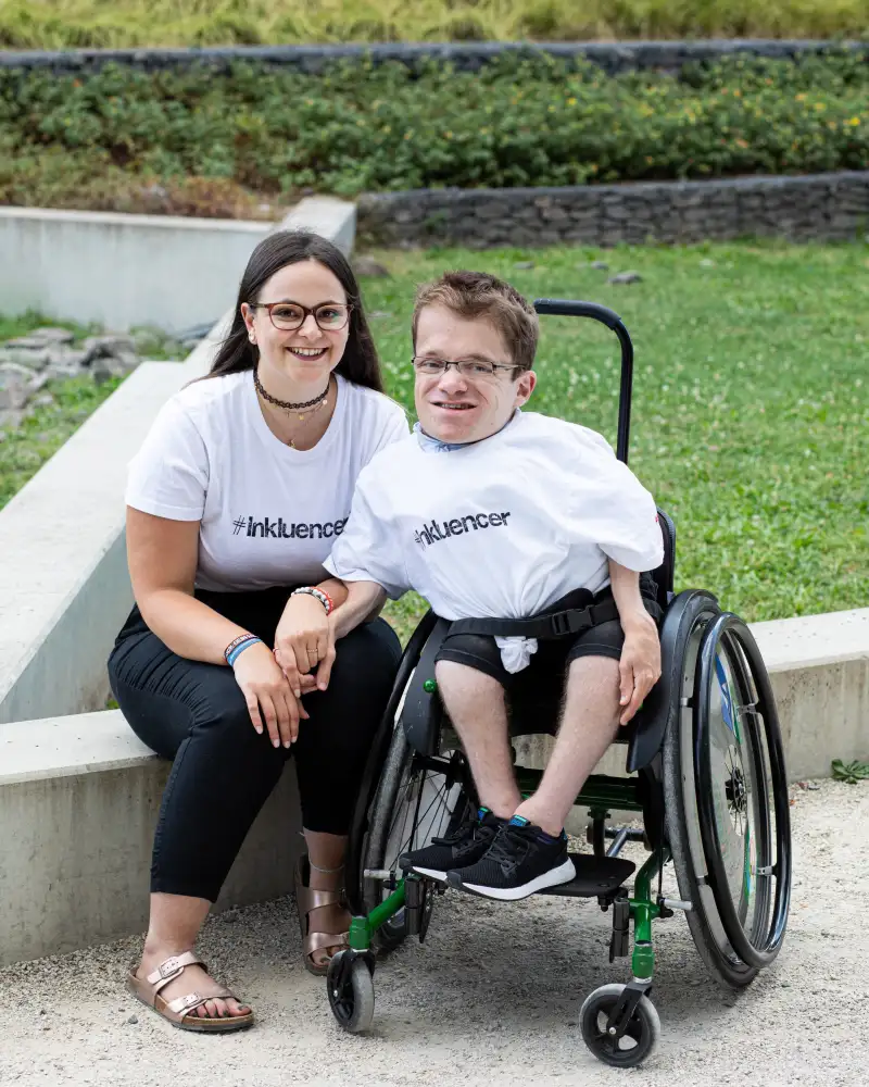 Max und Cristina sitzen in Inkluencer-T-Shirts im Freien.