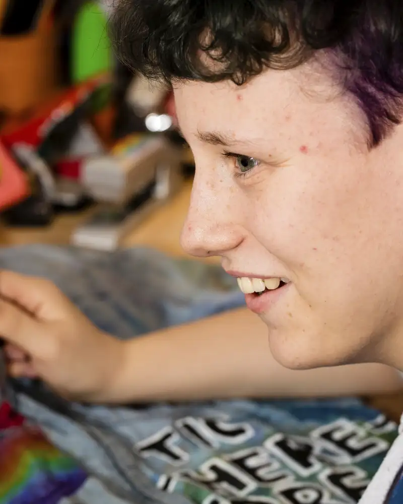 René, eine jugendliche Person mit kurzen, braunen Haaren, sitzt an einem Schreibtisch und malt mit einem Pinsel.