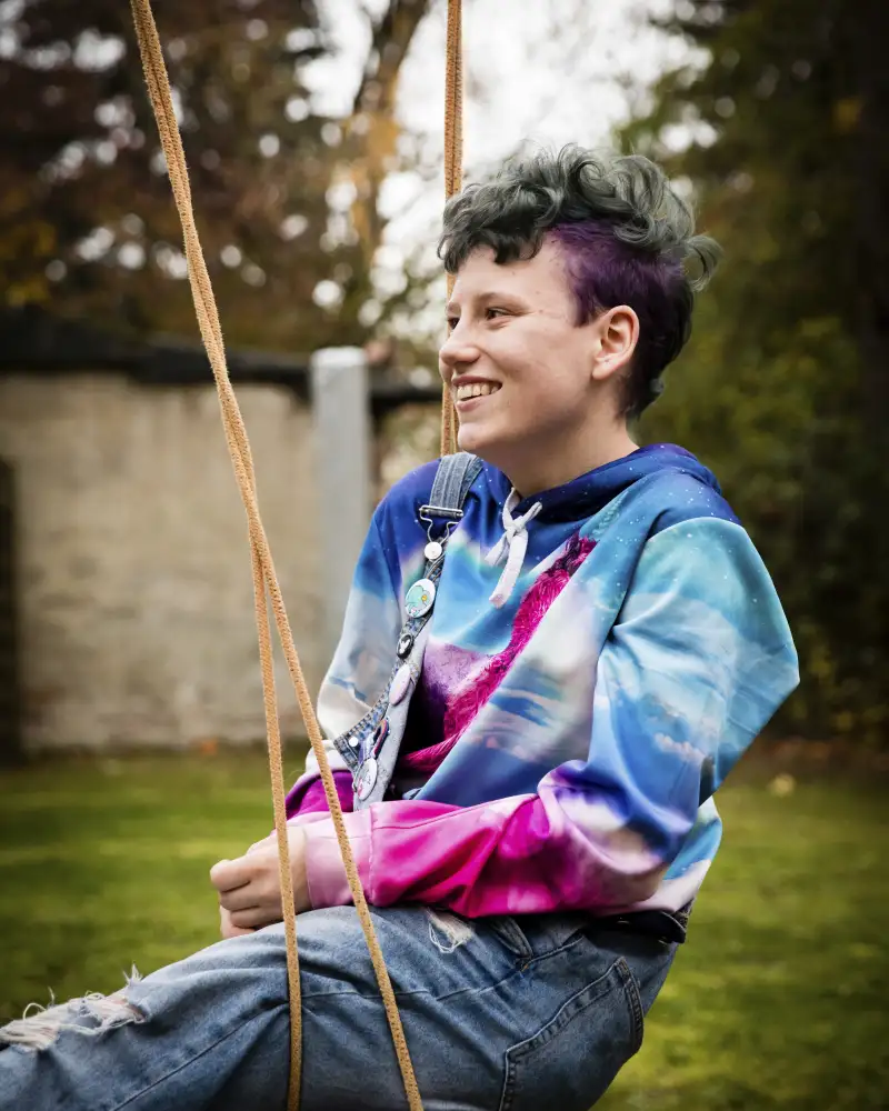 René sitzt in einem bunten Pullover auf einer Schaukel.