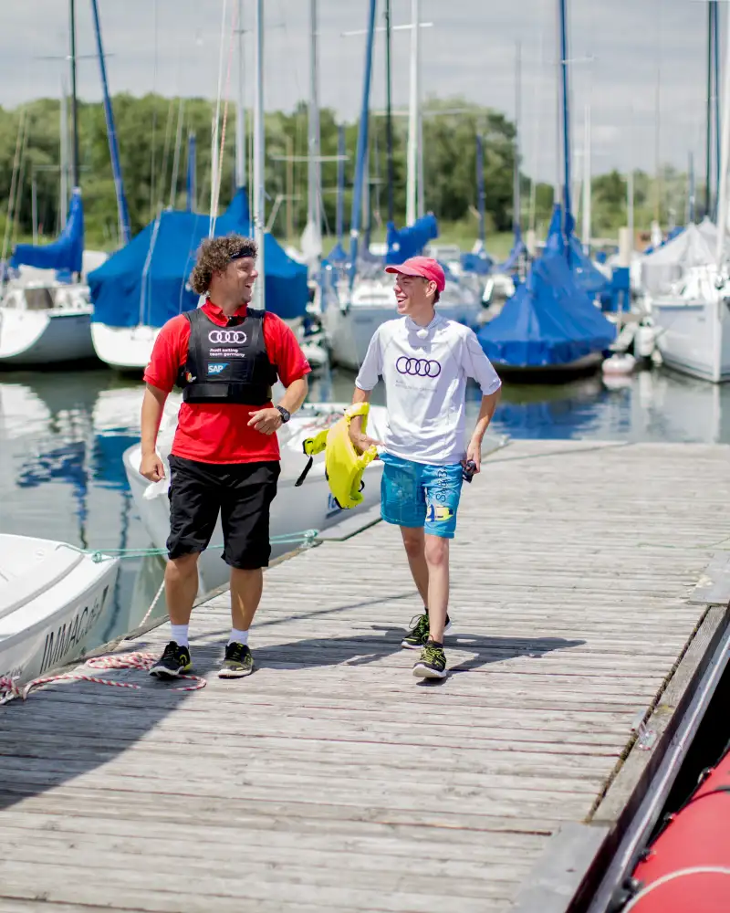 Zwei Männer laufen einen Boots-Steg entlang und lachen.