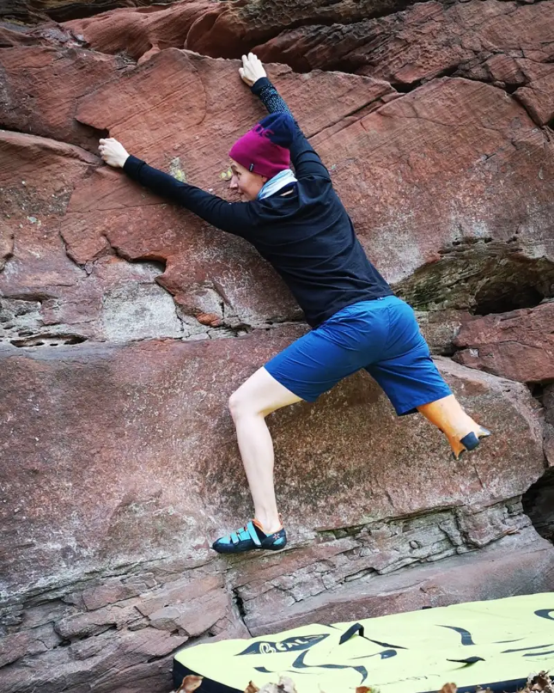 Eine junge unterschenkelamputierte Frau klettert in einer Felswand.