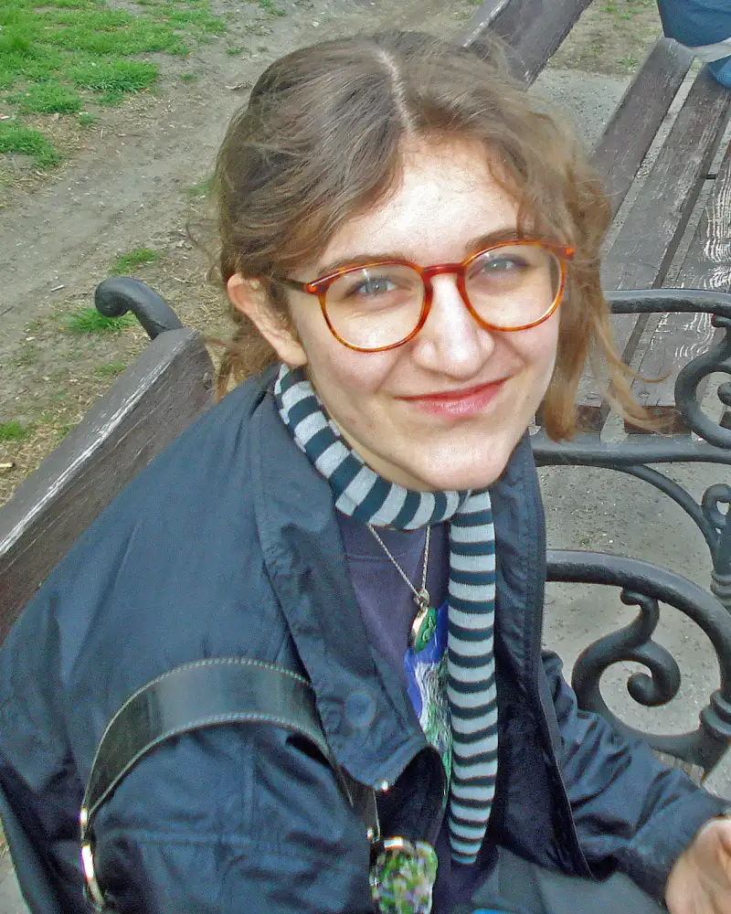 Porträt einer jungen Frau mit Brille auf einer Parkbank.