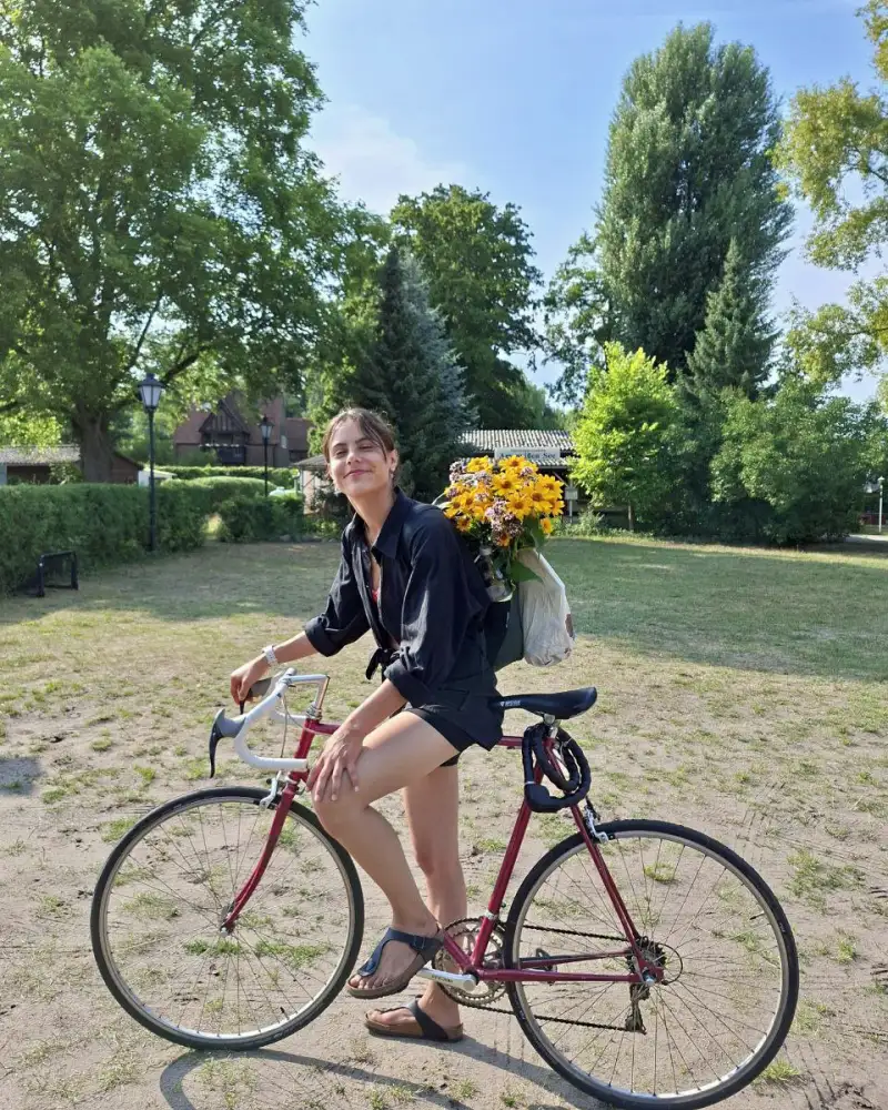 Eine junge Frau mit Rennrad. Auf dem Rücken trägt sie einen Rucksack mit Blumenstrauß.