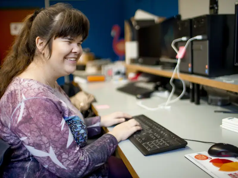 Eine junge Frau mit langen dunklen Haaren, die zu einem Pferdeschwanz gebunden sind, sitzt vor einer Computer-Tastatur.
