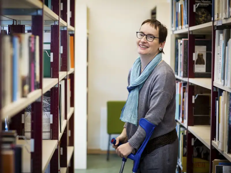 Agnes, eine 46-Jährige mit kurzen dunklen Haaren und Brille steht zwischen zwei Regalen.