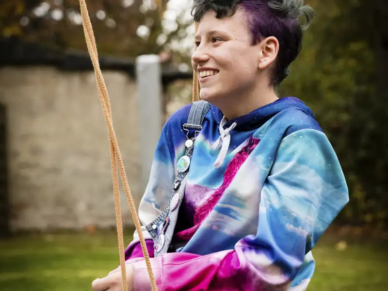 René sitzt in einem bunten Pullover auf einer Schaukel.
