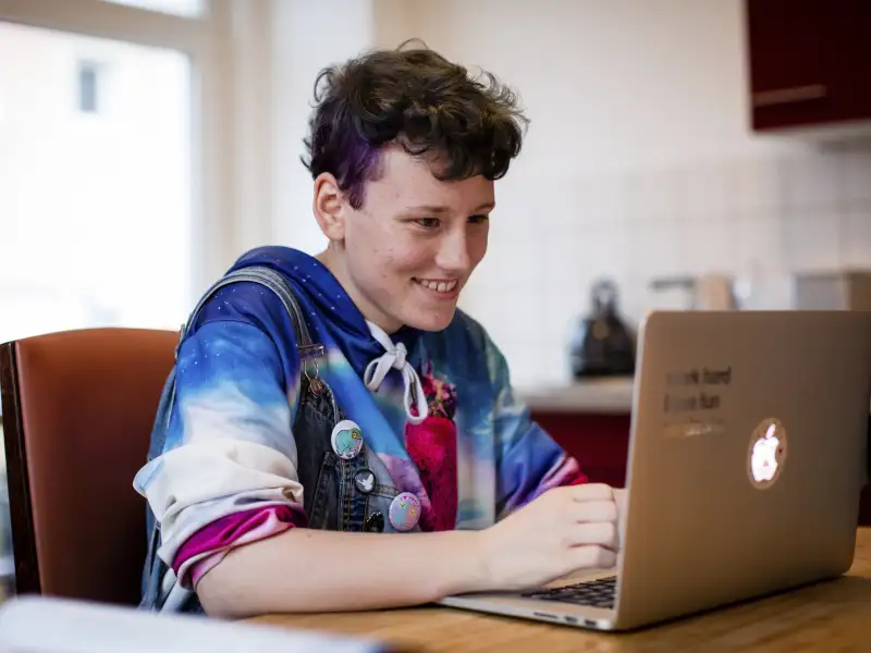 René sitzt an einem Küchentisch und tippt auf einem Laptop.