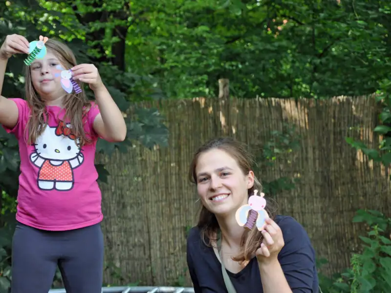 Ein Mädchen und eine junge Frau in einem Garten. Sie halten Selbstgebasteltes in der Hand.