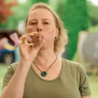 Gewinnerin Claudia - eine Frau mit mittellangen, blonden Haaren - steht in einem Garten und pustet eine Luftschlange.