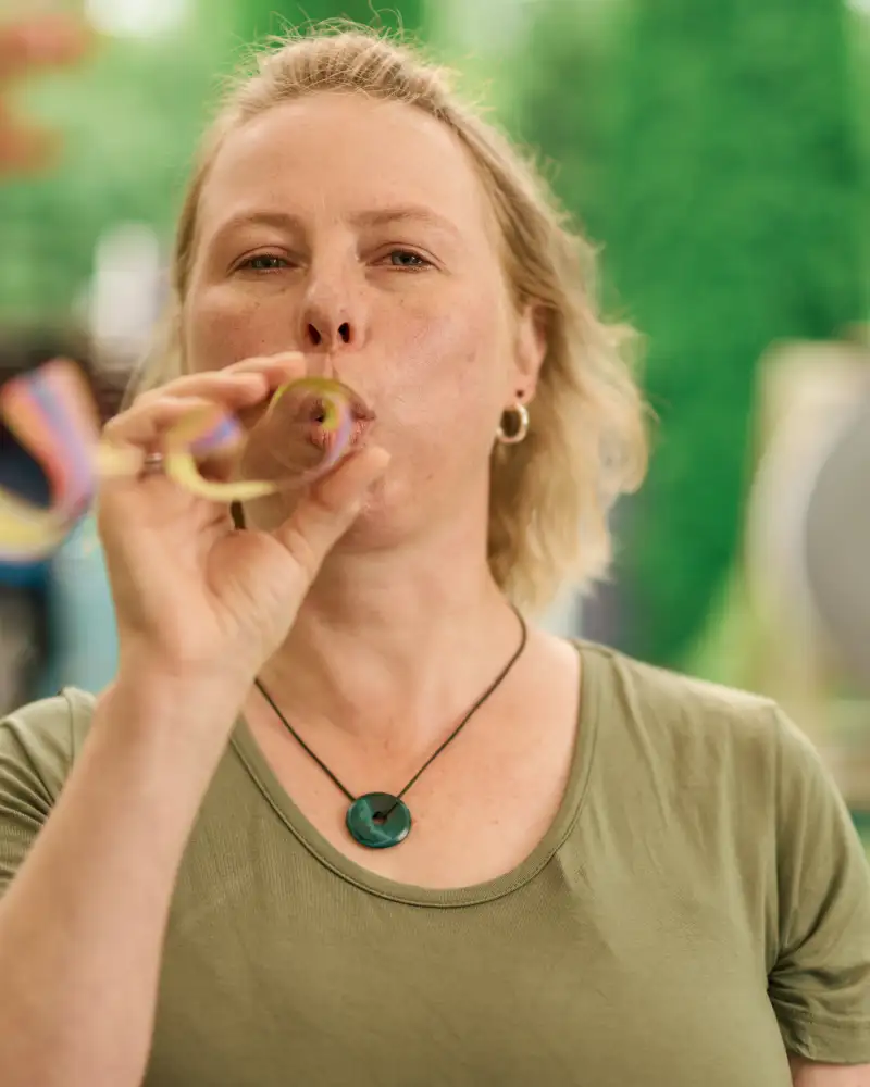 Gewinnerin Claudia - eine Frau mit mittellangen, blonden Haaren - steht in einem Garten und pustet eine Luftschlange.