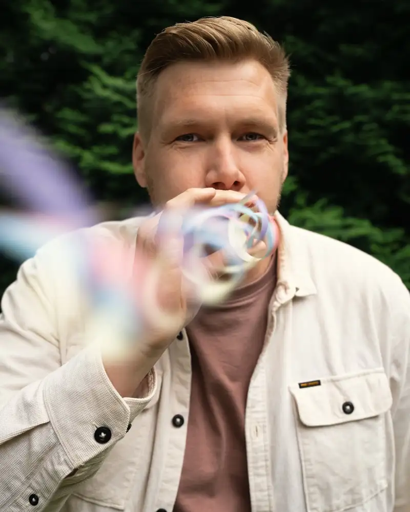 Aktion Mensch-Gewinner Daniel. Ein junger Mann mit kurzen blonden Haaren. Er pustet eine Luftschlange in Richtung Kamera.