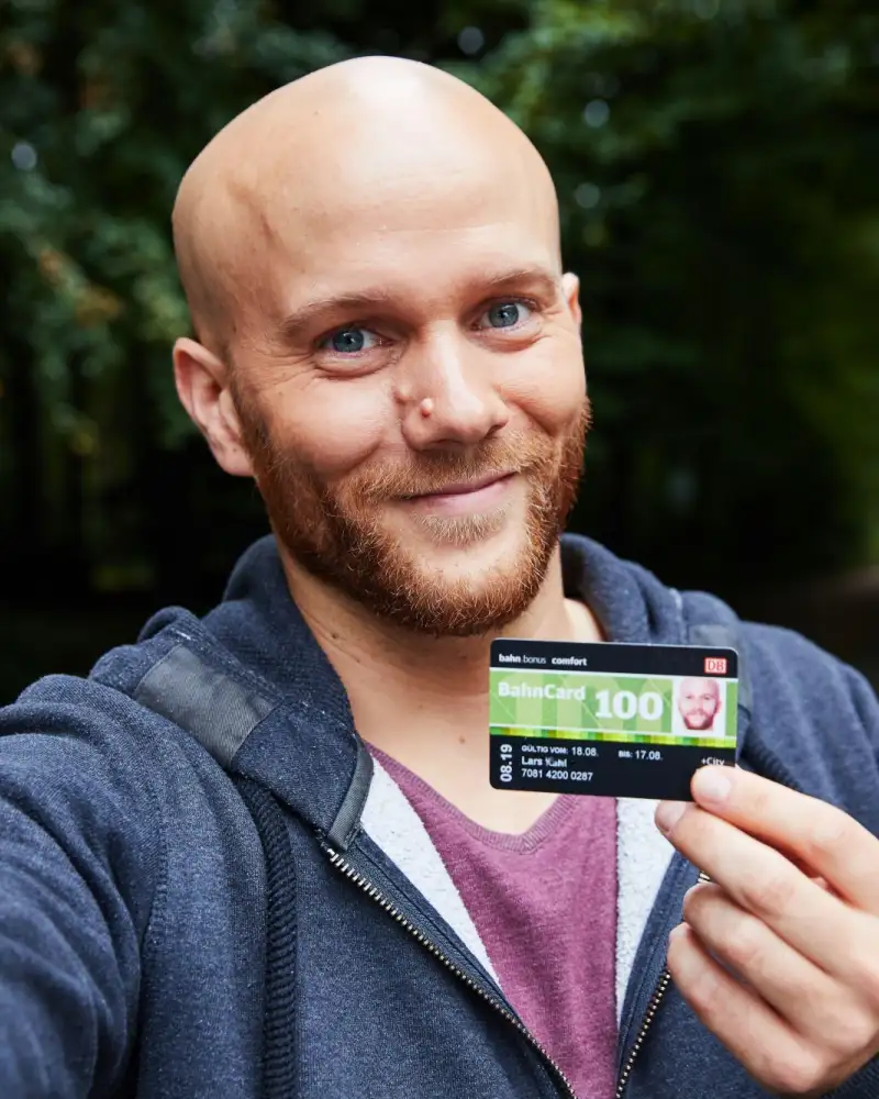 Aktion Mensch-Gewinner Lars - ein Mann mittleren Alters mit Glatze und Vollbart - hält lächelnd eine Bahncard in die Kamera.