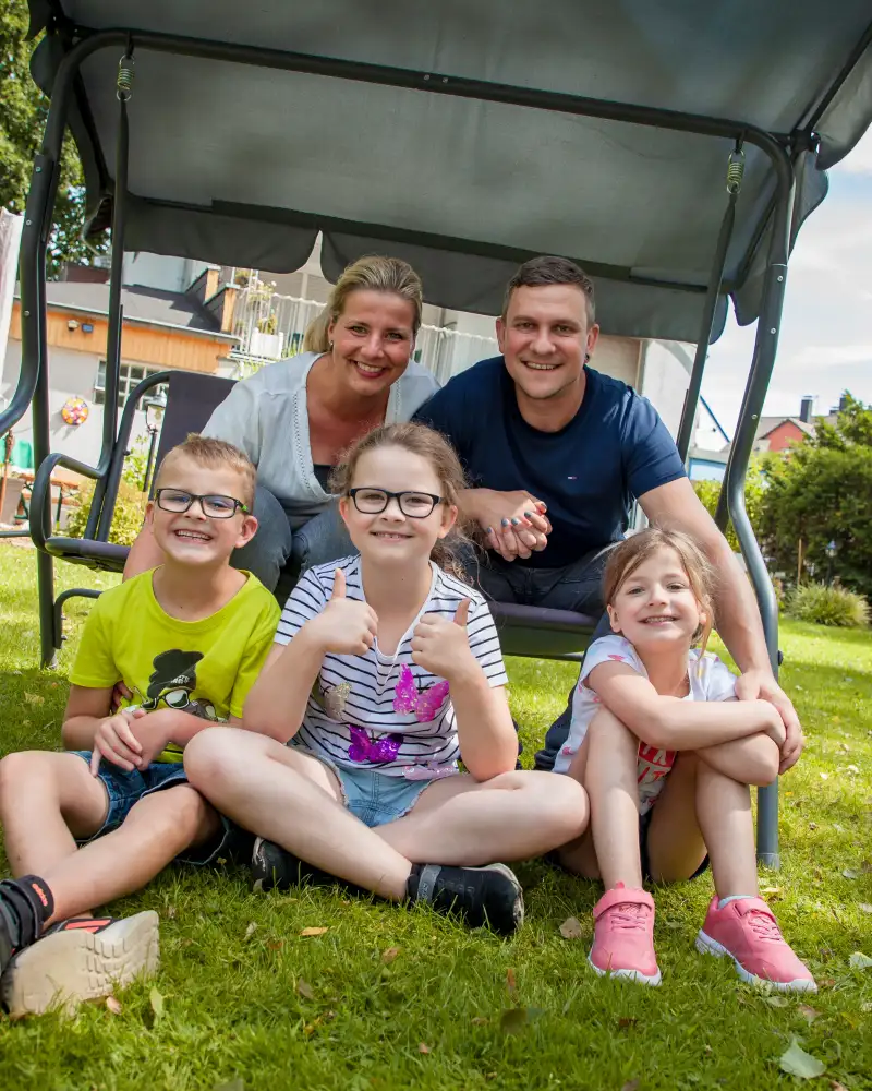 Aktion Mensch-Gewinner Marius mit Frau und Kindern im Garten. Die Eltern sitzen in einer Hollywood-Schaukel, die Kinder davor.