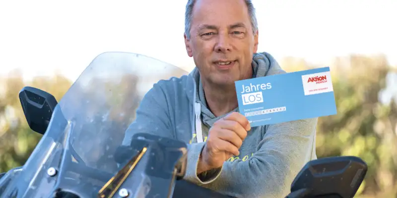 Aktion Mensch-Gewinner Jürgen sitzt auf einem Motorrad und hält ein Aktion Mensch-Los in der Hand.