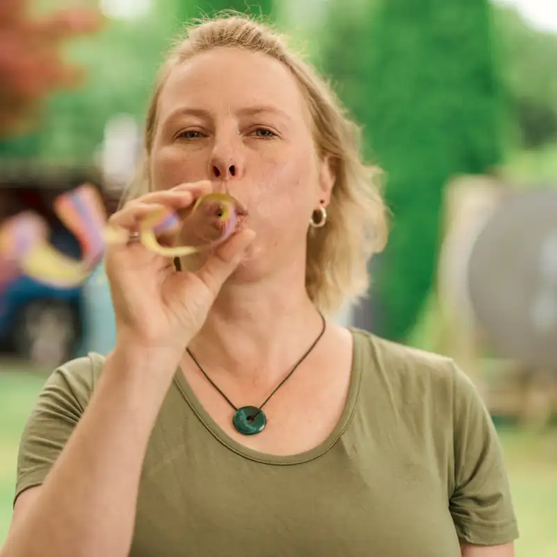 Gewinnerin Claudia - eine Frau mit mittellangen, blonden Haaren - steht in einem Garten und pustet eine Luftschlange.