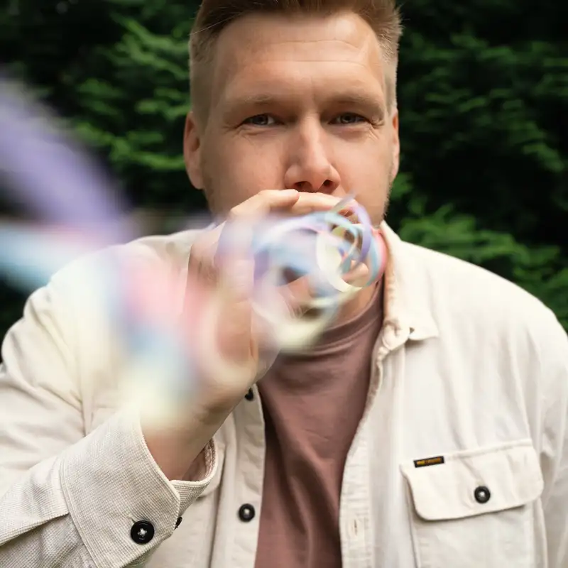 Aktion Mensch-Gewinner Daniel. Ein junger Mann mit kurzen blonden Haaren. Er pustet eine Luftschlange in Richtung Kamera.