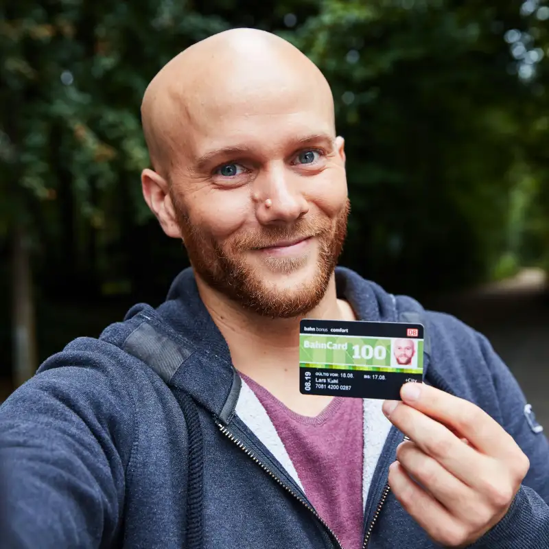 Aktion Mensch-Gewinner Lars - ein Mann mittleren Alters mit Glatze und Vollbart - hält lächelnd eine Bahncard in die Kamera.