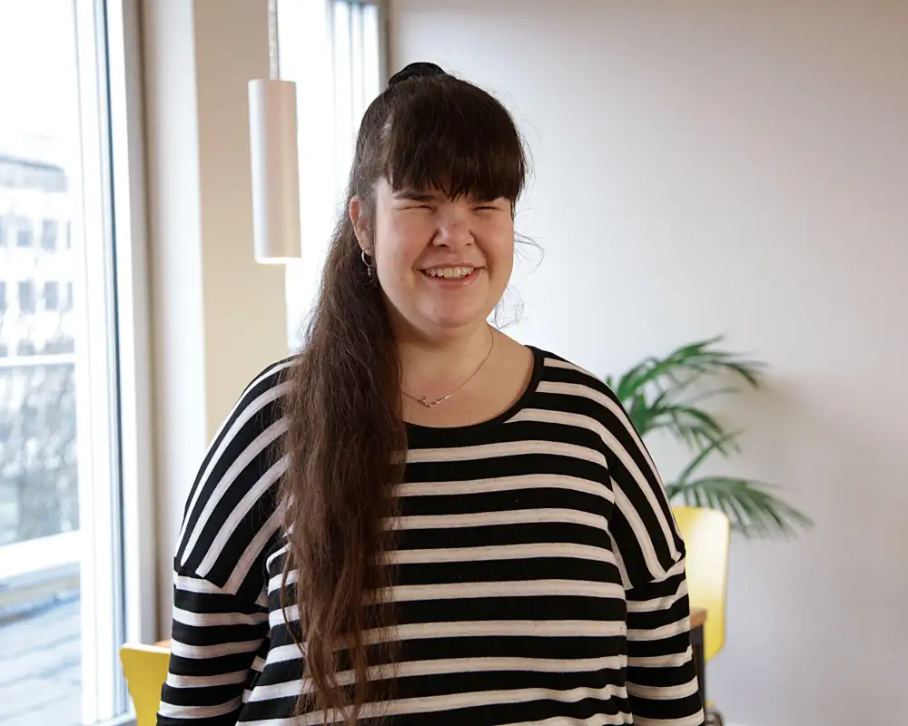 Eine junge Frau mit langem dunklem Pferdeschwanz und Ringelshirt lächelt in die Kamera.