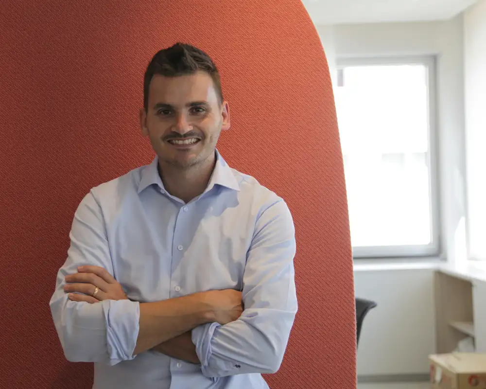 Nilson Reyes, ein Mann mit kurzen braunen Haaren und Schnurrbart. Er steht mit verschränkten Armen vor einer orangenen Wand.
