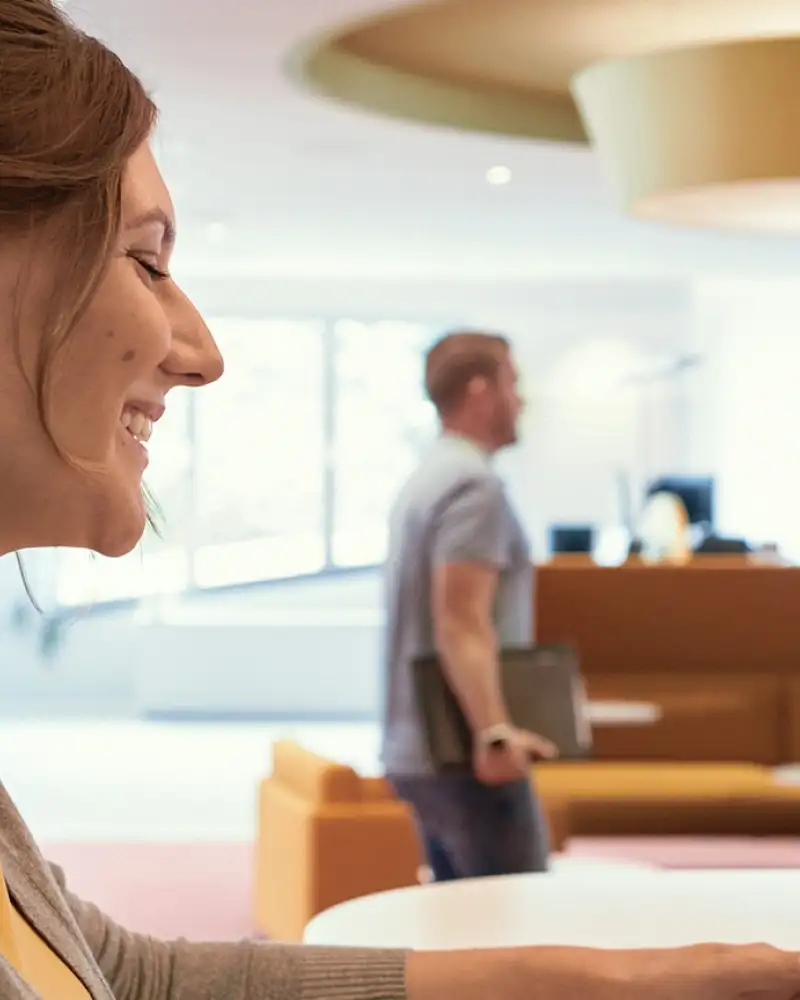 Eine junge Frau mit einem Cochlea-Implantat sitzt vor einem Laptop und nimmt an einer Videokonferenz teil.