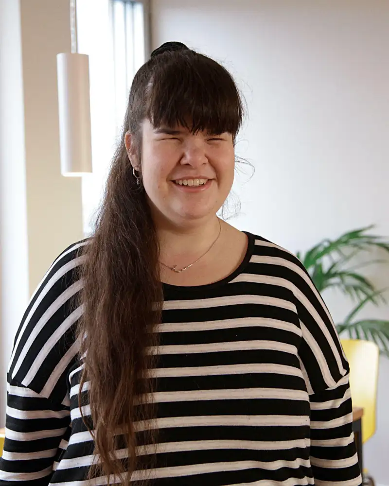 Eine junge Frau mit langem dunklem Pferdeschwanz und Ringelshirt lächelt in die Kamera.