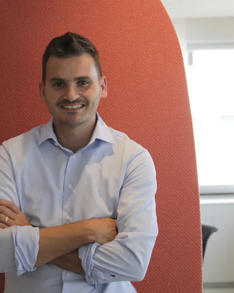 Nilson Reyes, ein Mann mit kurzen braunen Haaren und Schnurrbart. Er steht mit verschränkten Armen vor einer orangenen Wand.