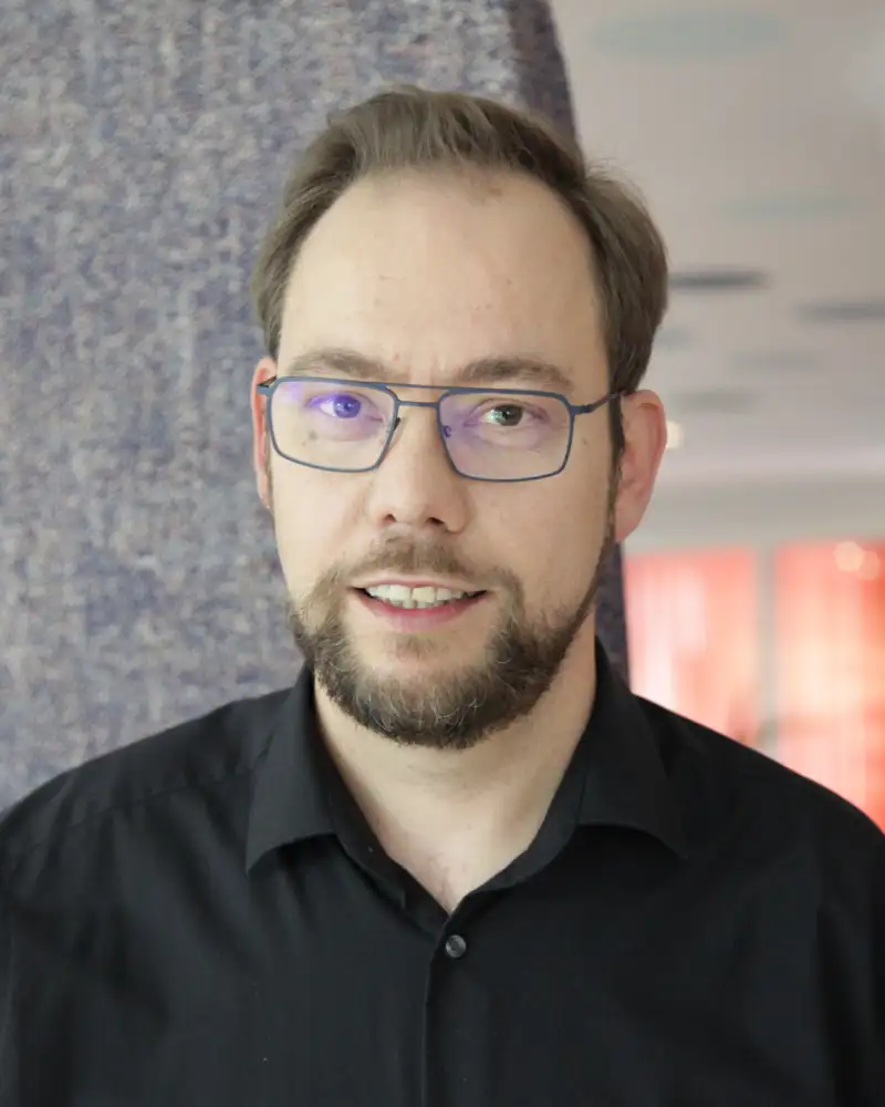 Alexander Westheide - ein Mann mit kurzen braunen Haaren, Bart, Schnäuzer und Brille steht in einem Aktion Mensch-Büro.