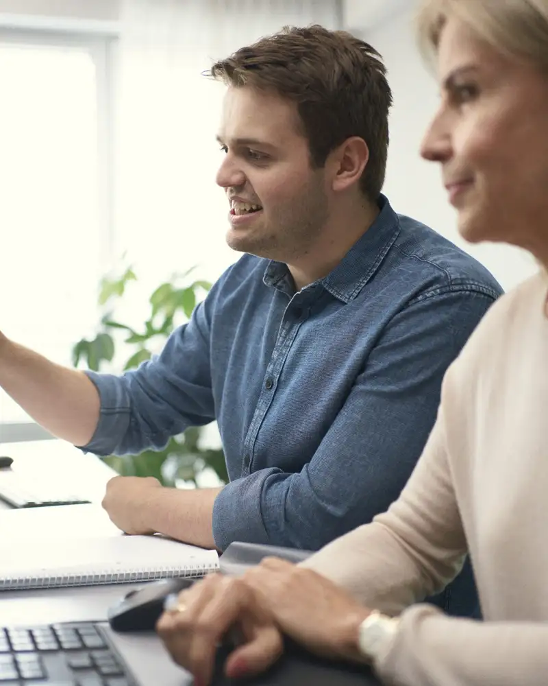 Ein junger Mann und eine blonde Frau sitzen gemeinsam vor einem Computerbildschirm und arbeiten an einem Code.