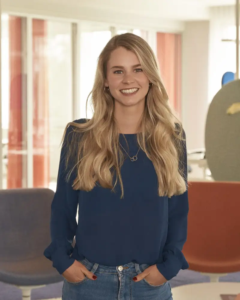 Annika Berglesow, eine junge, schmale Frau mit langen, blonden Haaren steht auf einer Bürofläche bei der Aktion Mensch.