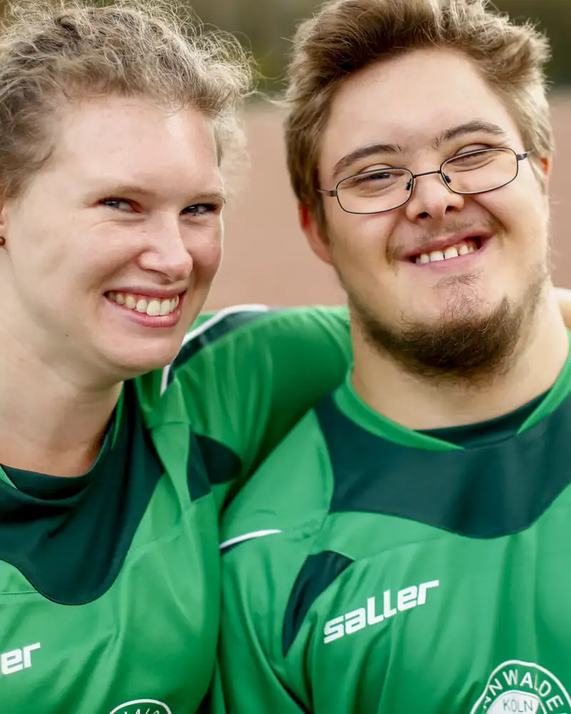 Eine junge Frau legt den Arm um einen jungen Mann, der eine geistige Einschränkung hat.
