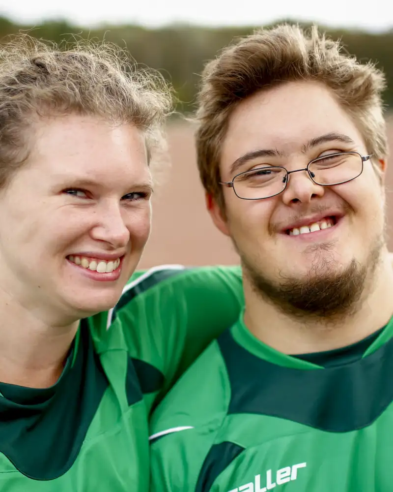 Eine junge Frau legt ihren Arm um einen jungen Mann mit geistiger Einschränkung.