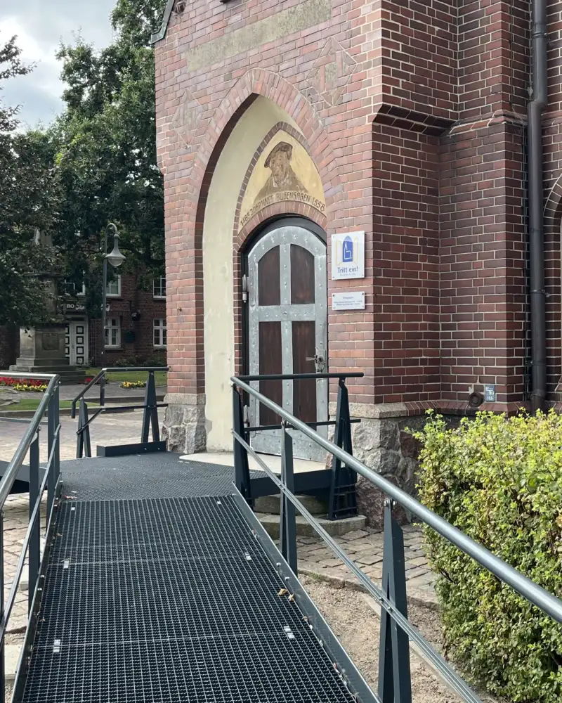 Eine lange Rampe führt zum Eingang einer Backsteinkirche.