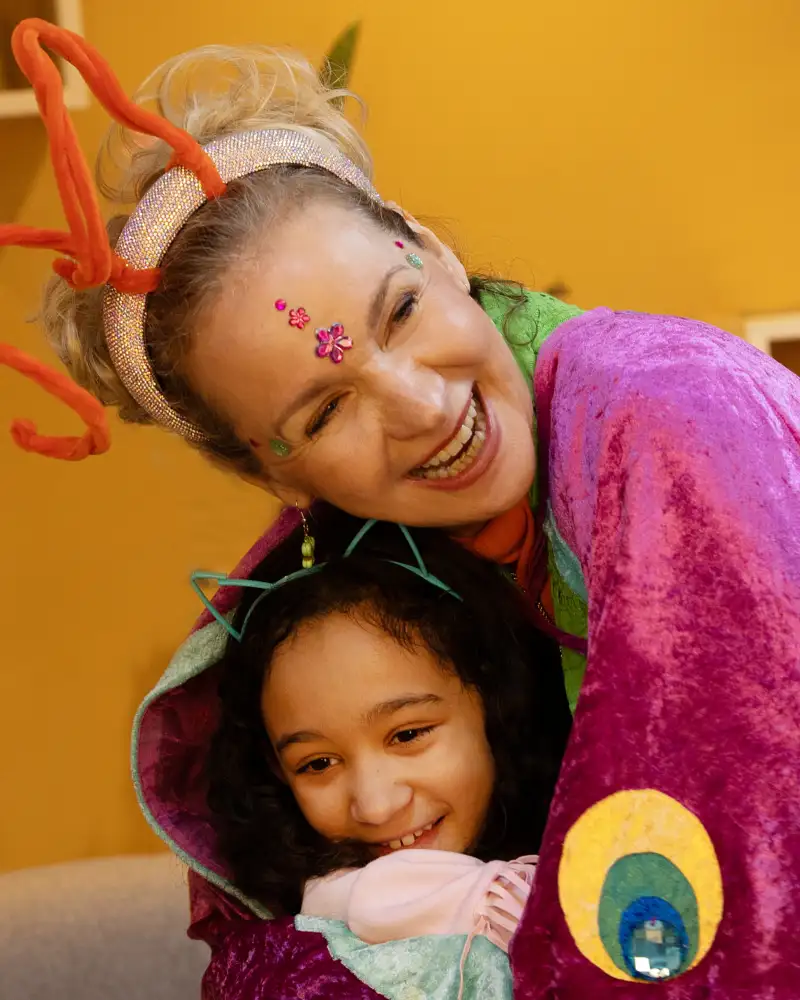 Eine Frau im Schmetterlingskostüm umarmt ein kleines Mädchen.