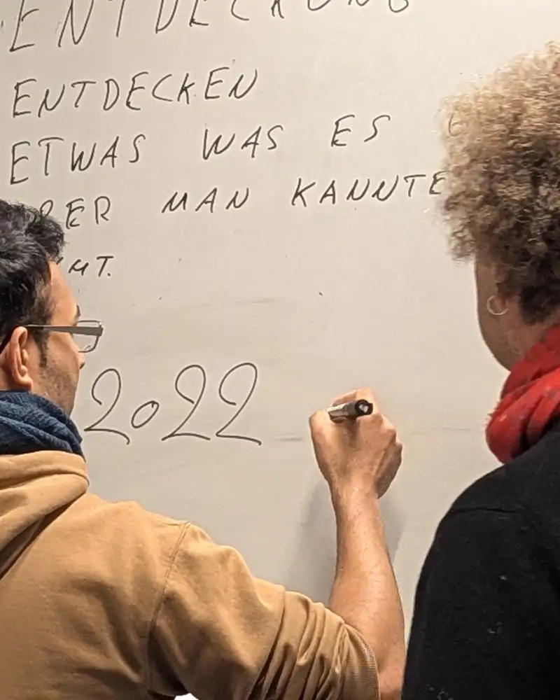 Eine Frau steht neben einem Mann, der Zahlen auf ein Flipchard schreibt.