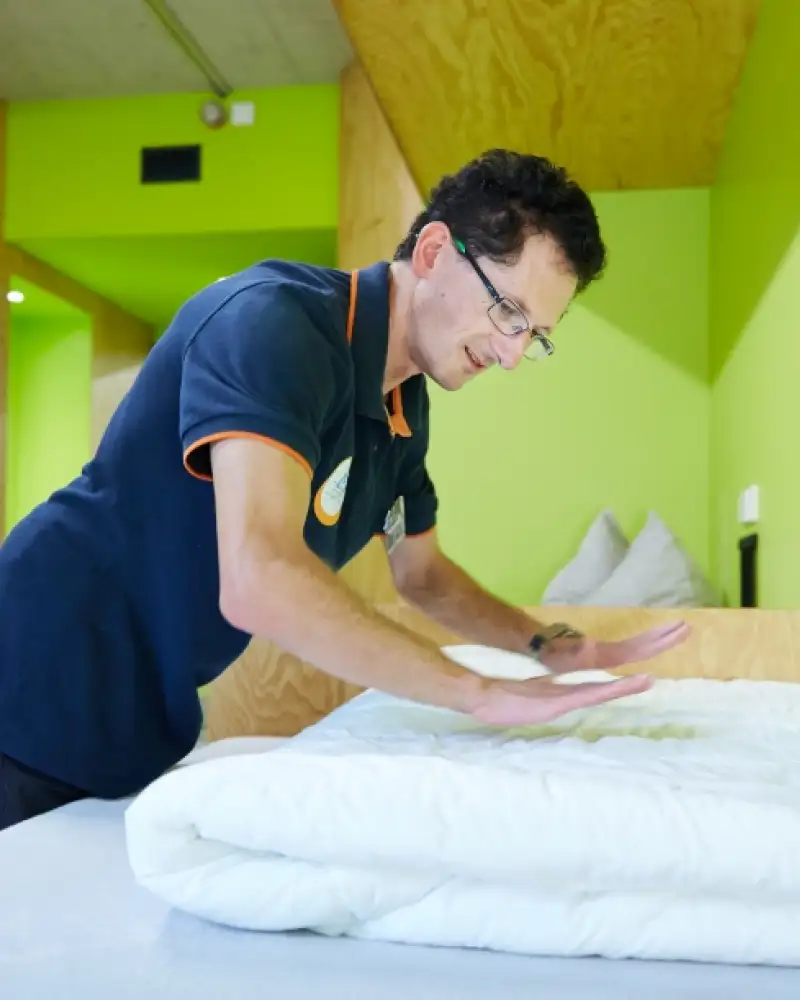 Ein Mann macht ein Bett in einem Mehrbettzimmer