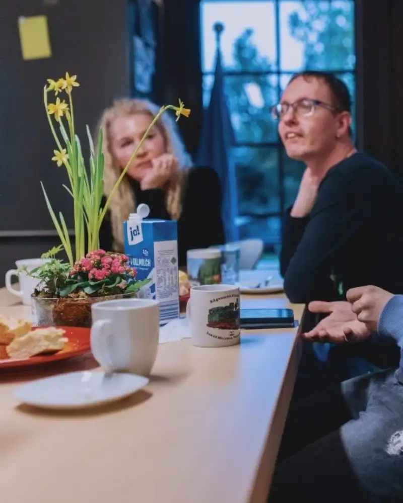 Menschen mit und ohne Behidnerung sitzen zusammen an einem Tisch