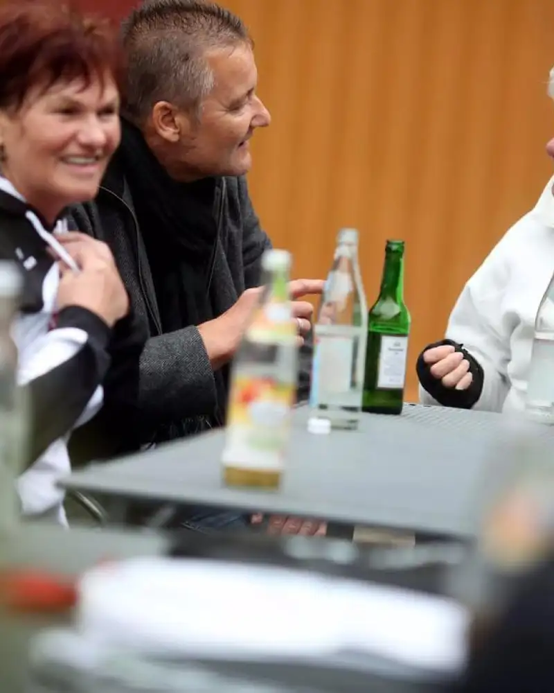Mehrere Erwachsene sitzen um einen Tisch. Auf dem Tisch stehen Glasflaschen.