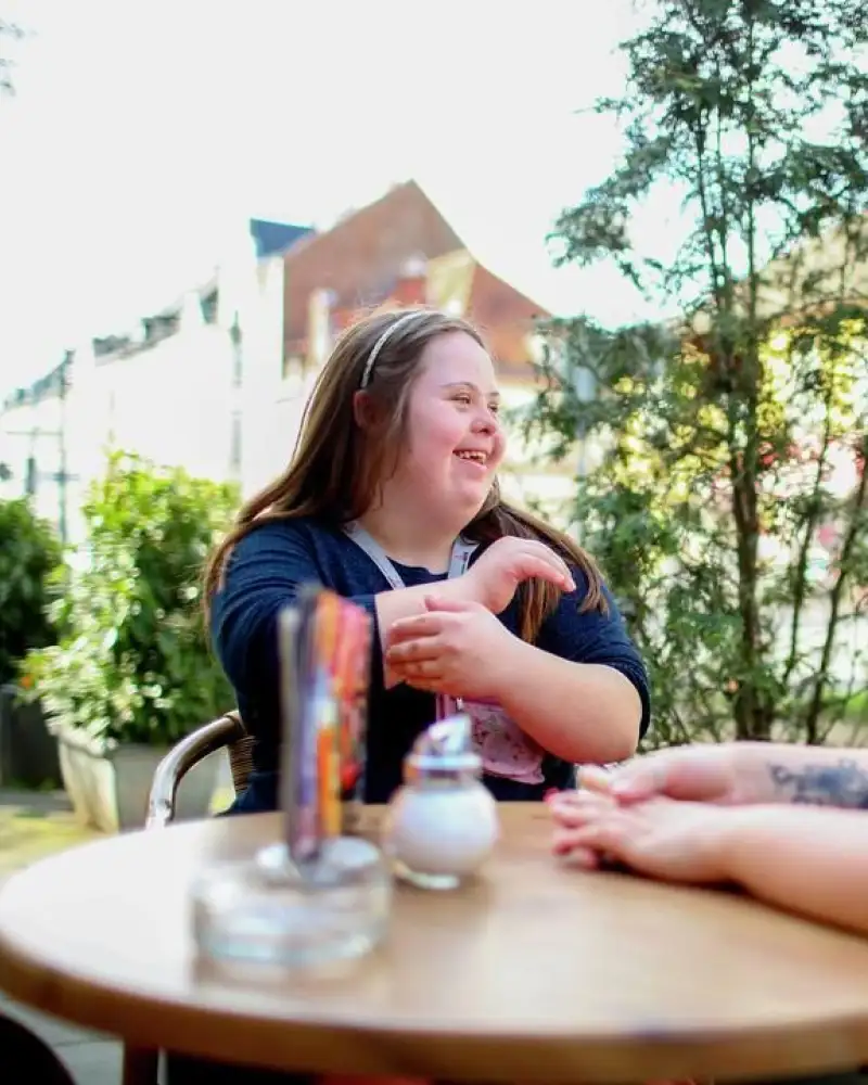Zwei junge Frauen sitzen zusammen in einem Straßencafé. Eine hat das Downsyndrom.