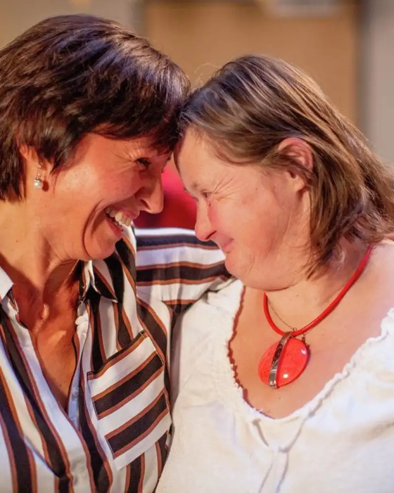 Zwei erwachsene Frauen haben sich im Arm und legen ihre Stirn aneinander.