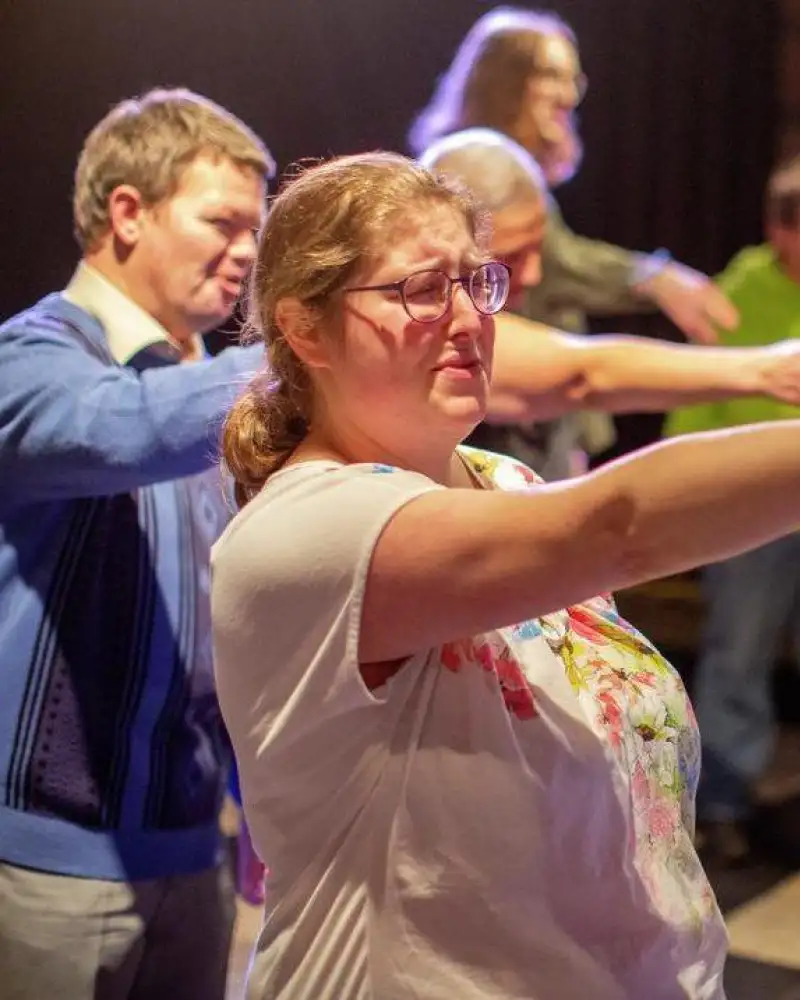 Mehrere Erwachsene  stehen in zwei Reihen und zeigen mit einem Arm nach vorne.