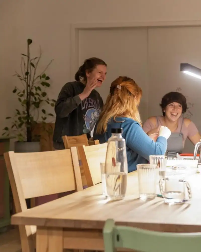 Fünf junge Frauen lachen an einem großen Tisch.