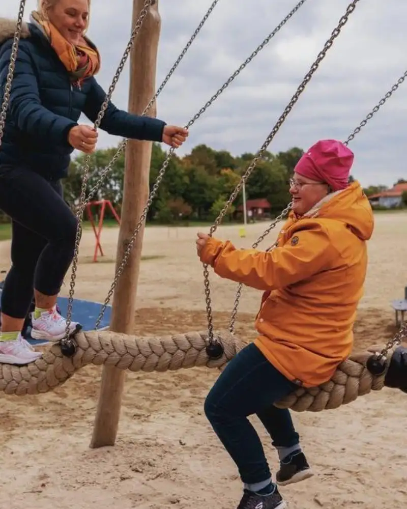 Eine junge Frau und eine Jugendliche auf einer Schaukel, die aus einem dicken Tau besteht.