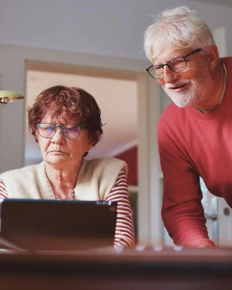 Eine ältere Dame schaut auf einen Laptop. Ein älterer Herr schaut ihr dabei über die Schulter.