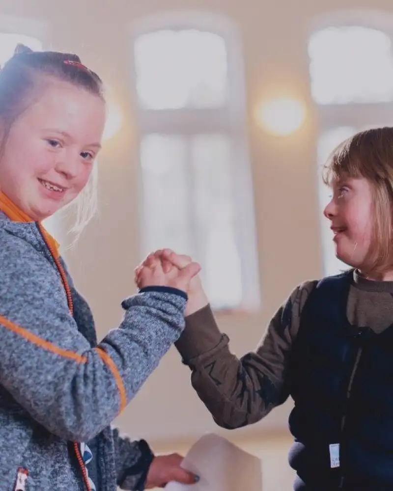 Zwei Mädchen mit Downsydrom halten sich an den Händen