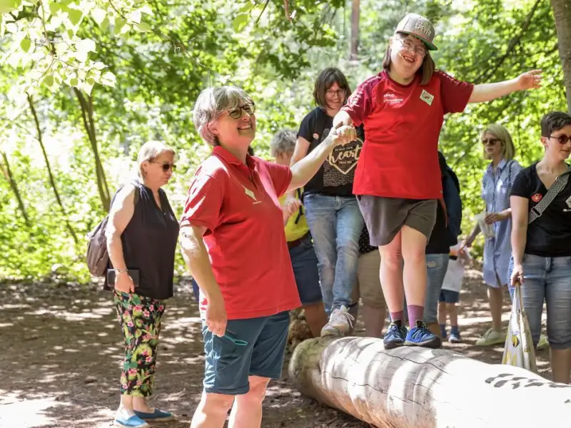 Ein Mädchen mit Down-Syndrom balanciert über einen Baumstamm.