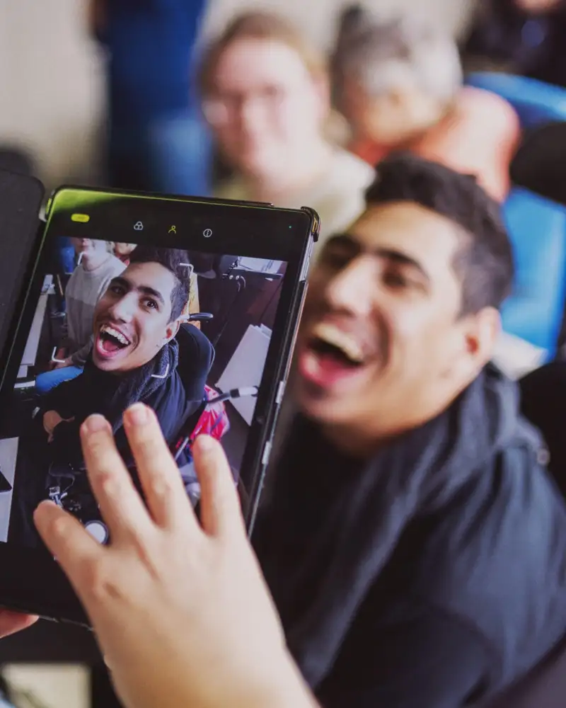 Ein Mann mit geistiger Behinderung hält ein Tablet hoch. Das Foto auf dem Bildschirm zeigt ihn selbst.