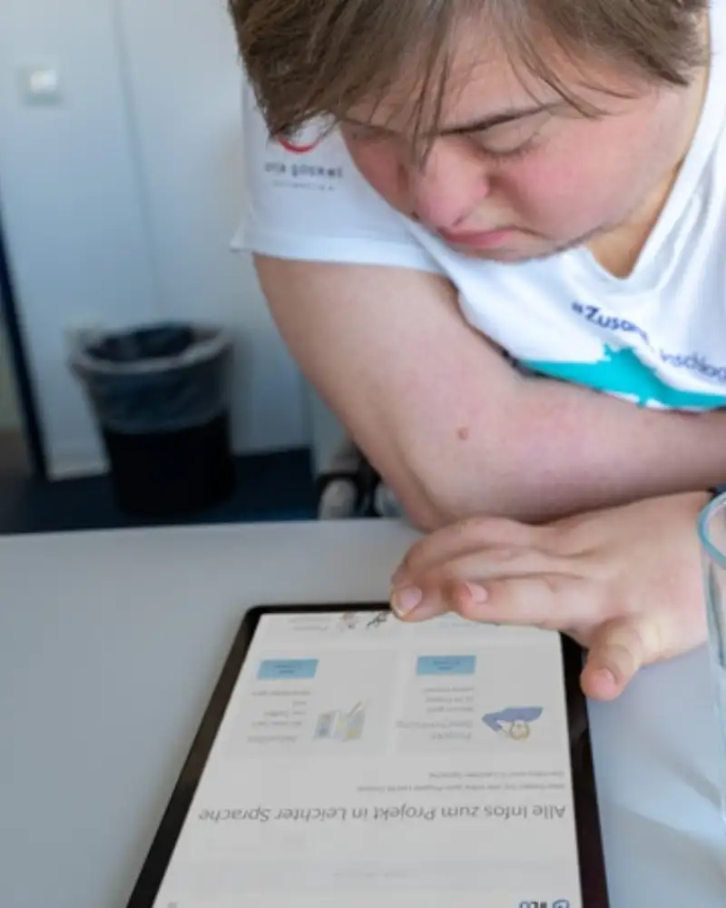 Ein junger Mann mit Downsyndrom tippt auf ein Tablet.
